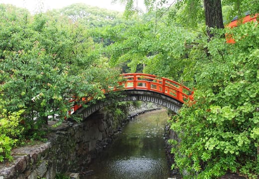 A vermilion arched bridge over the stone lined Mitarashi stream at Shimogamo Shrine, Kyoto