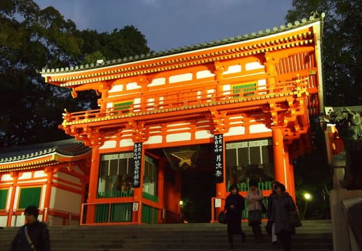 The vermilion west gate of Yasaka Shrine lit at dusk above its stone steps, Kyoto