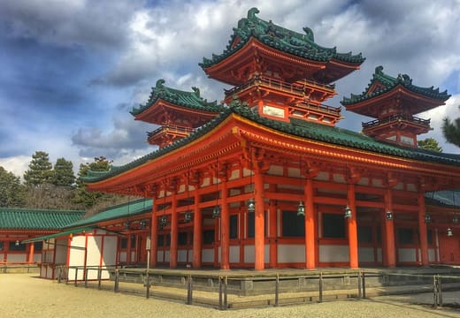 The vermilion and green halls of Heian Shrine under a cloudy sky