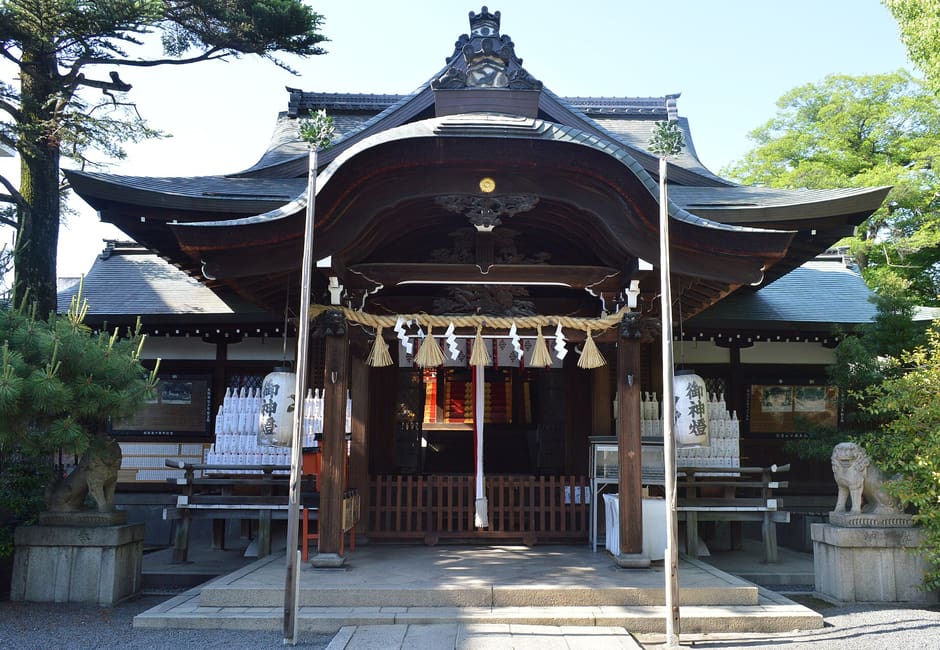 The main hall of Kumano Shrine in Kyoto, with its curved roof, shimenawa rope and stone guardian lions