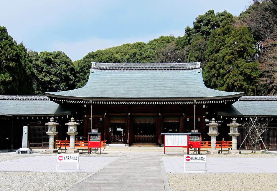 The worship hall of Kyoto Ryozen Gokoku Shrine behind its gravel courtyard and stone lanterns, wooded hillside above