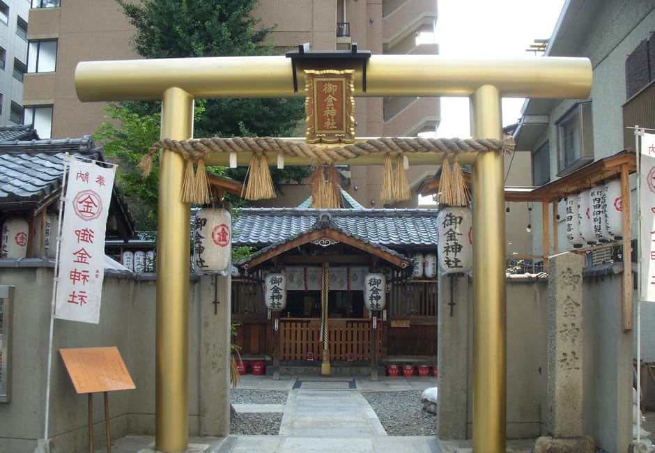 The gold torii of Mikane Shrine with its name plaque and straw rope, the small hall and lanterns behind it