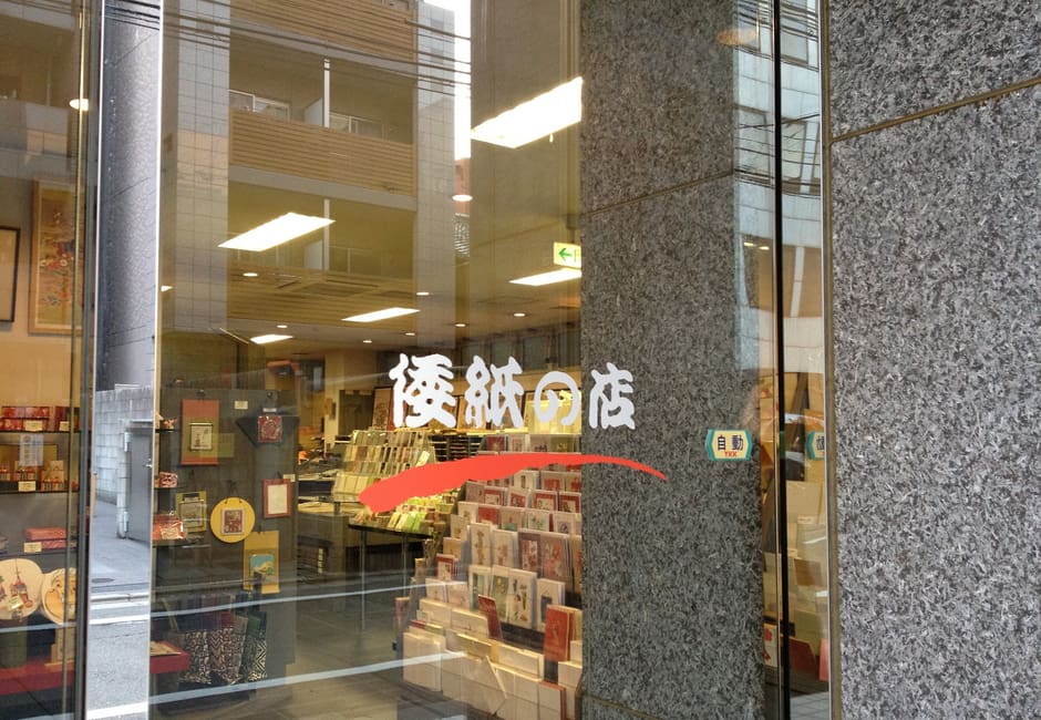The glass door of Morita Washi lettered with its shop name, racks of washi cards and paper goods behind it