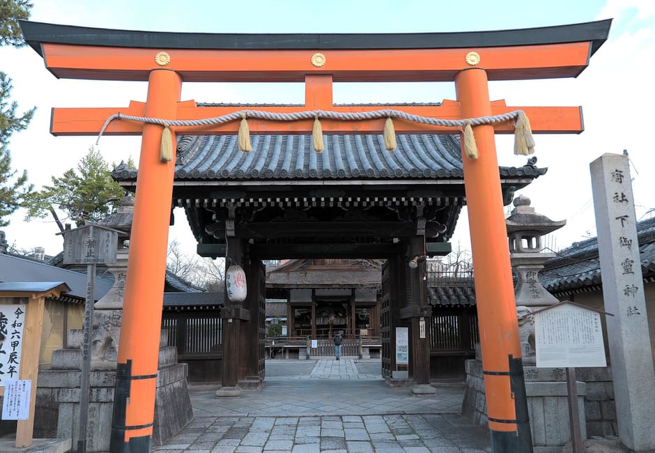 The vermilion torii of Shimogoryo Shrine in front of its roofed gate, with the shrine's stone name pillar beside it