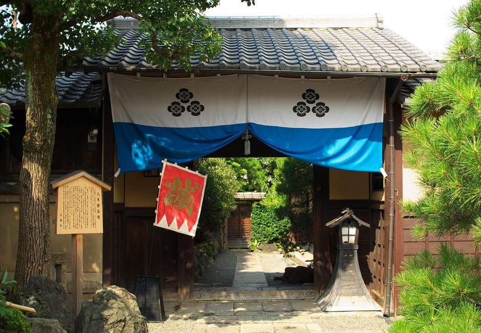The gate of Yagi House in Mibu, hung with a blue and white curtain bearing the family crest and a red Makoto banner