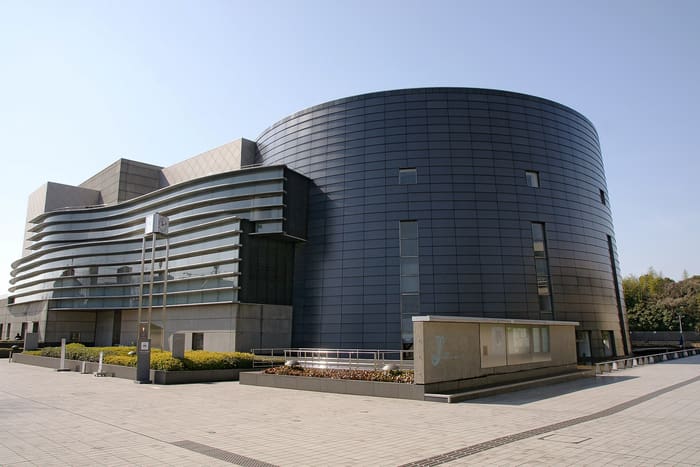 The curved dark metal wall of Kyoto Concert Hall in Kitayama beside a paved plaza